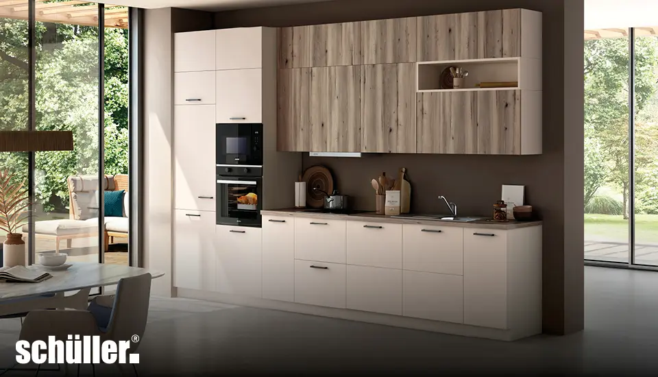 Zeitlose Schüller Küche mit cremefarbenen Unterschränken, Oberschränken in Holzoptik, integrierten Elektrogeräten und großer Fensterfront mit Blick ins Grüne